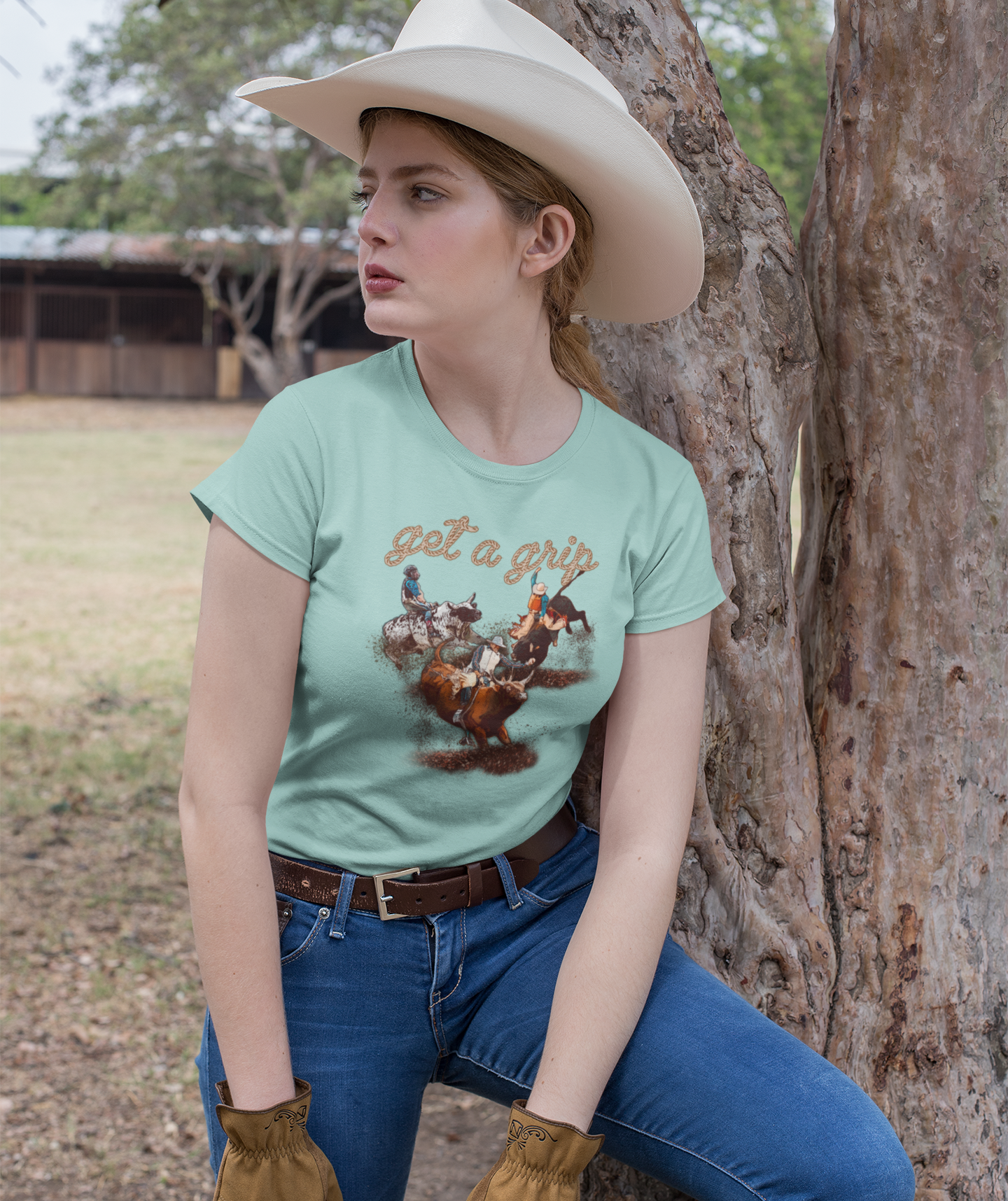 A cowgirl taking a short rest by a tree. She is wearing a dusty blue shirt and work gloves.