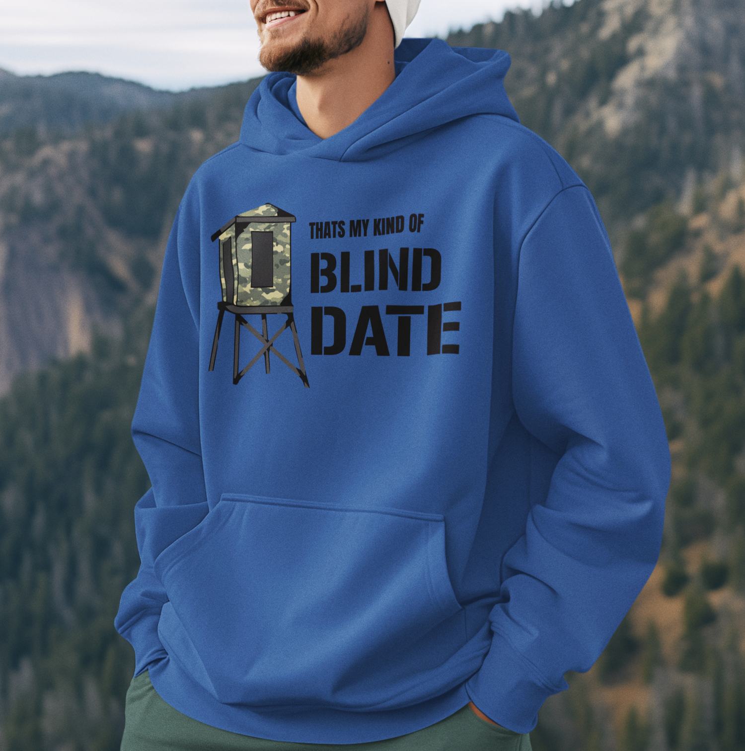 A man standing at the summit of a mountain wearing a blue sweatshirt.