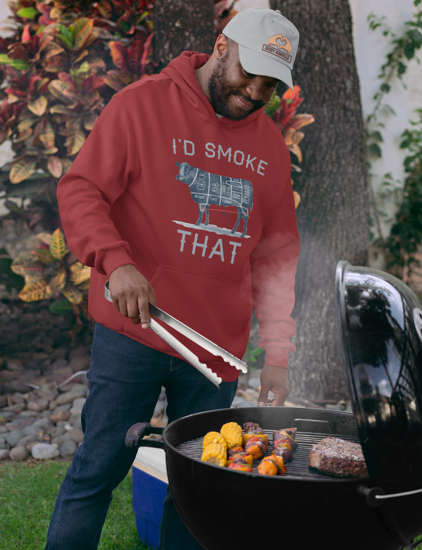 A dad wearing a dad hat and sweatshirt grilling dinner on a charcoal grill.
