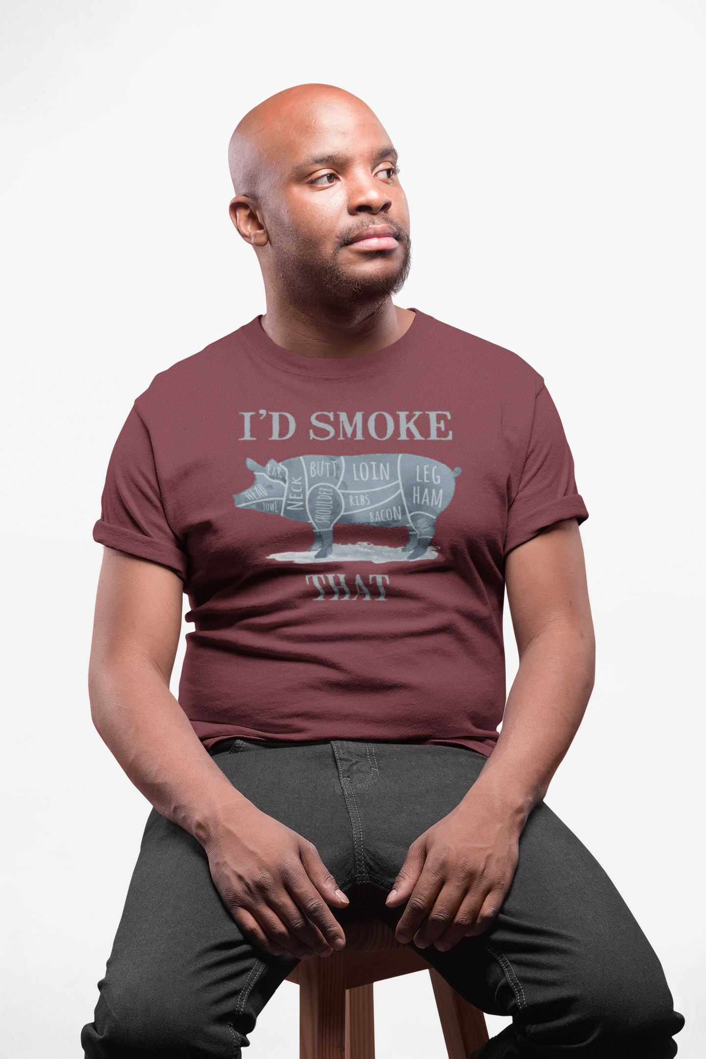 Man wearing a maroon t-shirt with a graphic design and text, sitting on a stool against a plain background.